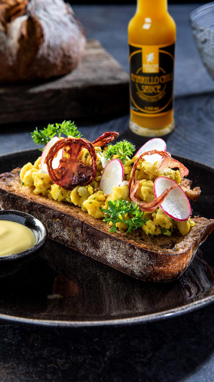 Ein rustikales Brot belegt mit veganem Eiersalat aus Fusilli und Kichererbsen, garniert mit Radieschenscheiben und Kräutern, dazu eine Seite veganer Mayonnaise.